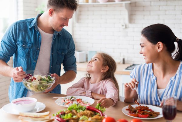 Un uomo e una donna sorridono davanti a un tavolo con insalata e verdure, promuovendo l'alimentazione sana per i bambini.