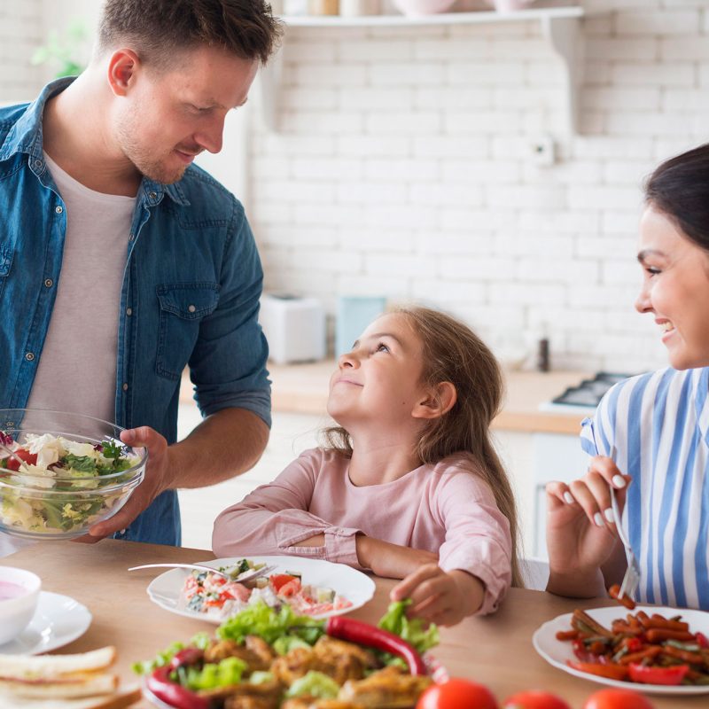 Un uomo e una donna sorridono davanti a un tavolo con insalata e verdure, promuovendo l'alimentazione sana per i bambini.