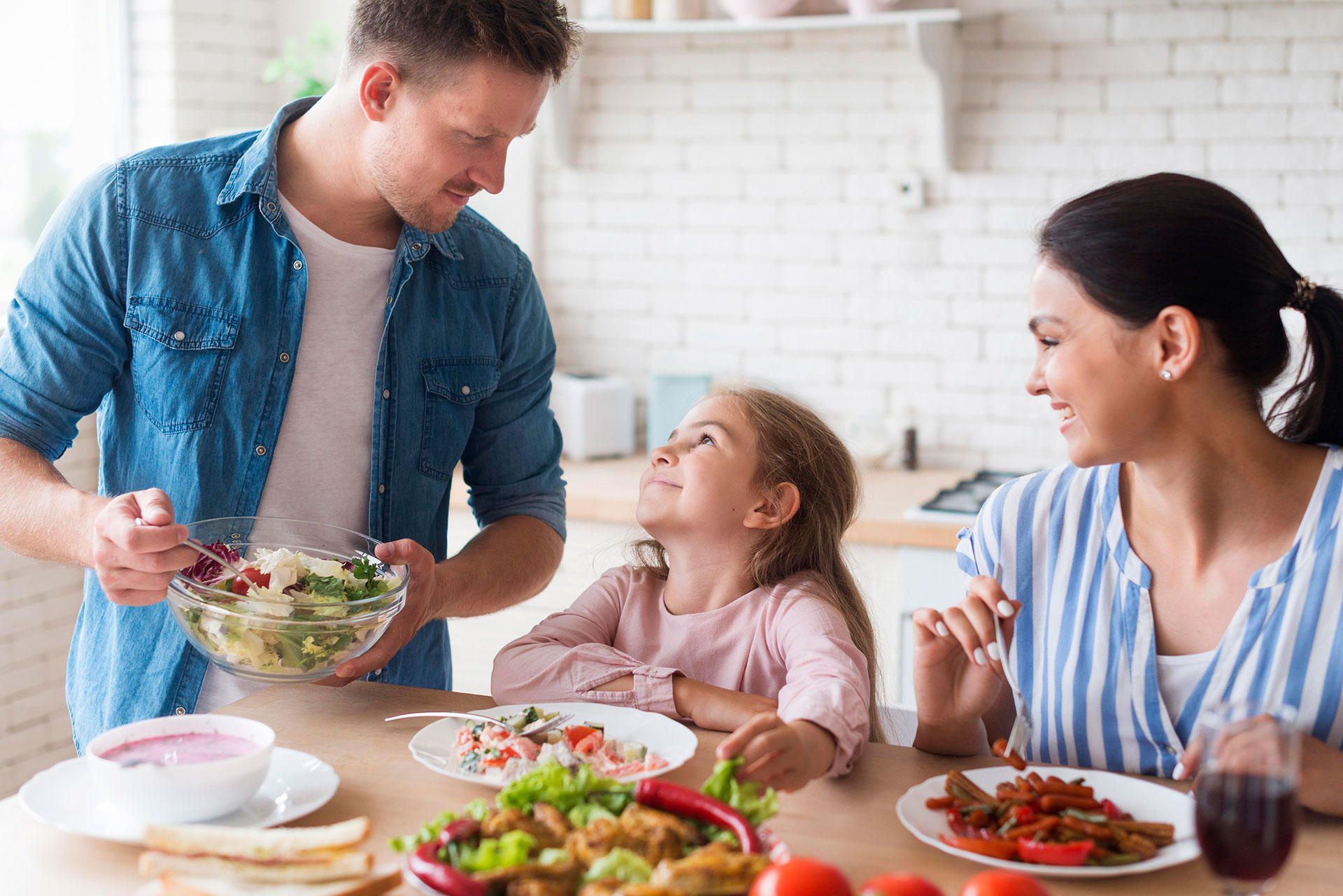 Un uomo e una donna sorridono davanti a un tavolo con insalata e verdure, promuovendo l'alimentazione sana per i bambini.